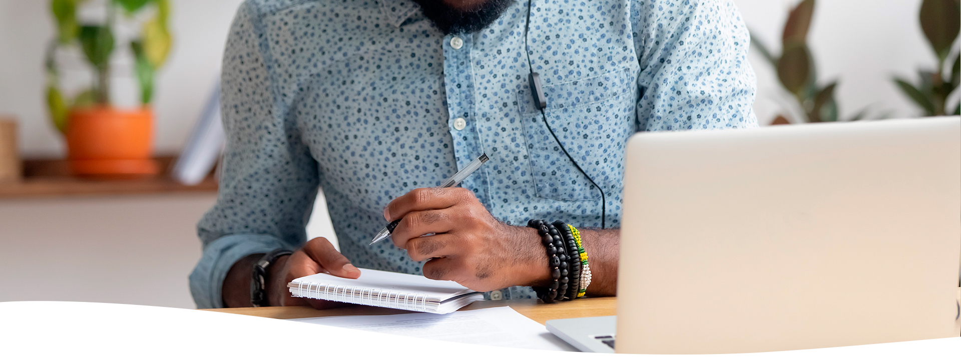 Hombre con audífonos utilizando una laptop y escribiendo notas en sus documentos.