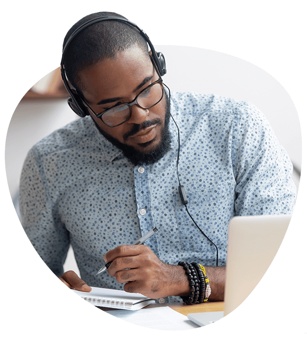 Hombre con audífonos utilizando una laptop y escribiendo notas en sus documentos